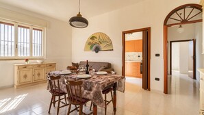 Zona pranzo con tavolo imbandito per quattro persone, divano e ventaglio decorativo a parete.