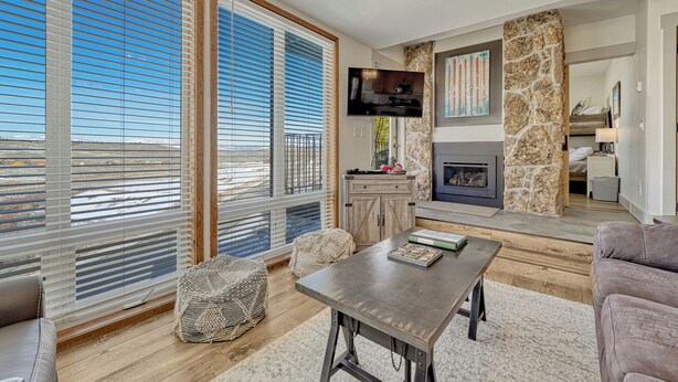 A spacious living area with large windows, a fireplace, and a television.