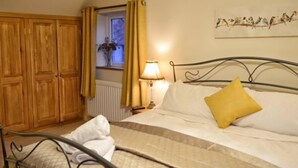 A bedroom with a bed, a nightstand, a lamp, a window with curtains, and a wooden wardrobe. - Cosy & Spacious Cottage in Scenic Village With Pub (Ashbourne)