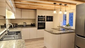 A modern kitchen with wooden beams, built-in ovens, a granite countertop, and pendant lighting. - Cosy & Spacious Cottage in Scenic Village With Pub (Ashbourne)