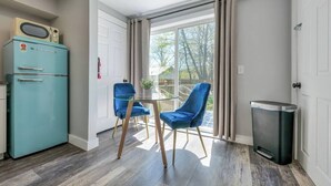 Una habitación con un refrigerador verde azulado, dos sillas azules, una mesa de vidrio y vistas a través de un ventanal grande.
