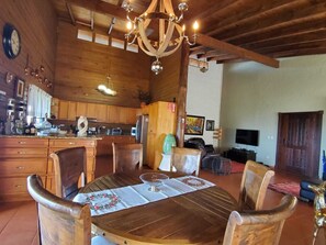 A rustic wooden interior with a dining table set for four, surrounded by wooden chairs. A chandelier hangs from the ceiling, and a television is mounted on the wall. - Cozy modern rustic house on jamaca de Dios (Jarabacoa)