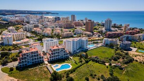 An aerial view of a coastal residential area with multiple high-rise buildings, a large swimming pool, and a beach in the background.