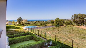 A pool area with a view of the sea, surrounded by well-maintained gardens and a fenced area.