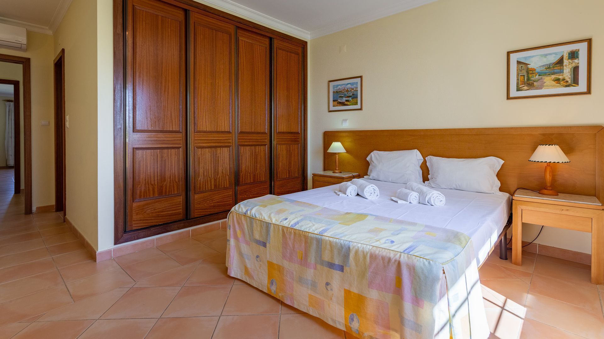 A hotel room with a large bed, wooden wardrobe, two bedside tables, and two wall-mounted lamps.