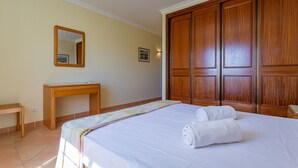 A hotel room with a bed, a wooden wardrobe, a small desk, and a mirror.