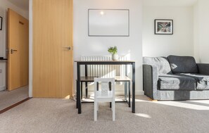 A room with a wooden door, a white chair, a small table, a grey sofa, a radiator, and a framed picture on the wall. - Bright and Airy 1BD Flat in Trendy Peckham (London)
