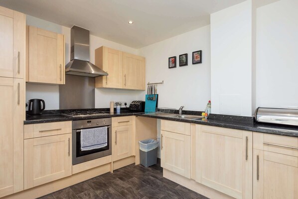 A modern kitchen with light wood cabinets, stainless steel appliances, and a black countertop.