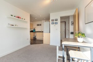 Experience a clean and minimalist living space with a spacious living area, kitchen, dining area, and a hallway leading to a bedroom.