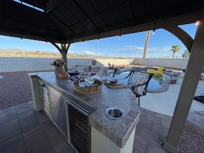 An outdoor kitchen area with a built-in grill, seating, and a view of a swimming pool.