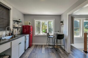 A compact kitchen with a red refrigerator, a window with a view, and a small dining area with two chairs.