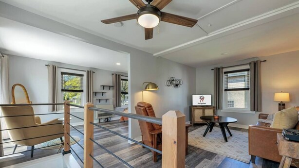A modern living room with a staircase, a ceiling fan, and a television displaying a logo.