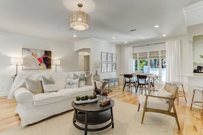 A modern living room with a white sofa, a round coffee table, and a dining area with a table and chairs.