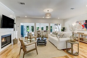A spacious living room with a fireplace, white furniture, and a large painting.