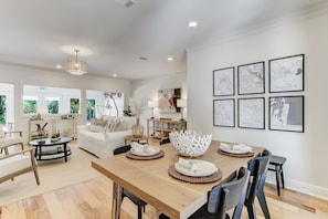 A modern living room with a dining area, white furniture, and framed maps on the wall.