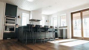 A modern kitchen with a central island, built-in oven, and bar stools.