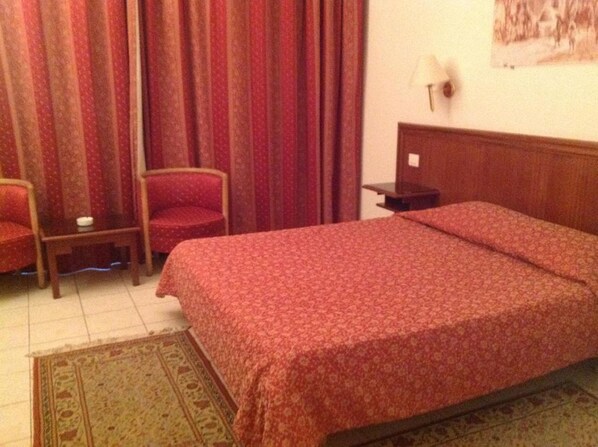 A hotel room with a bed, a chair, a nightstand, and curtains. - El Hana International (Tunis)