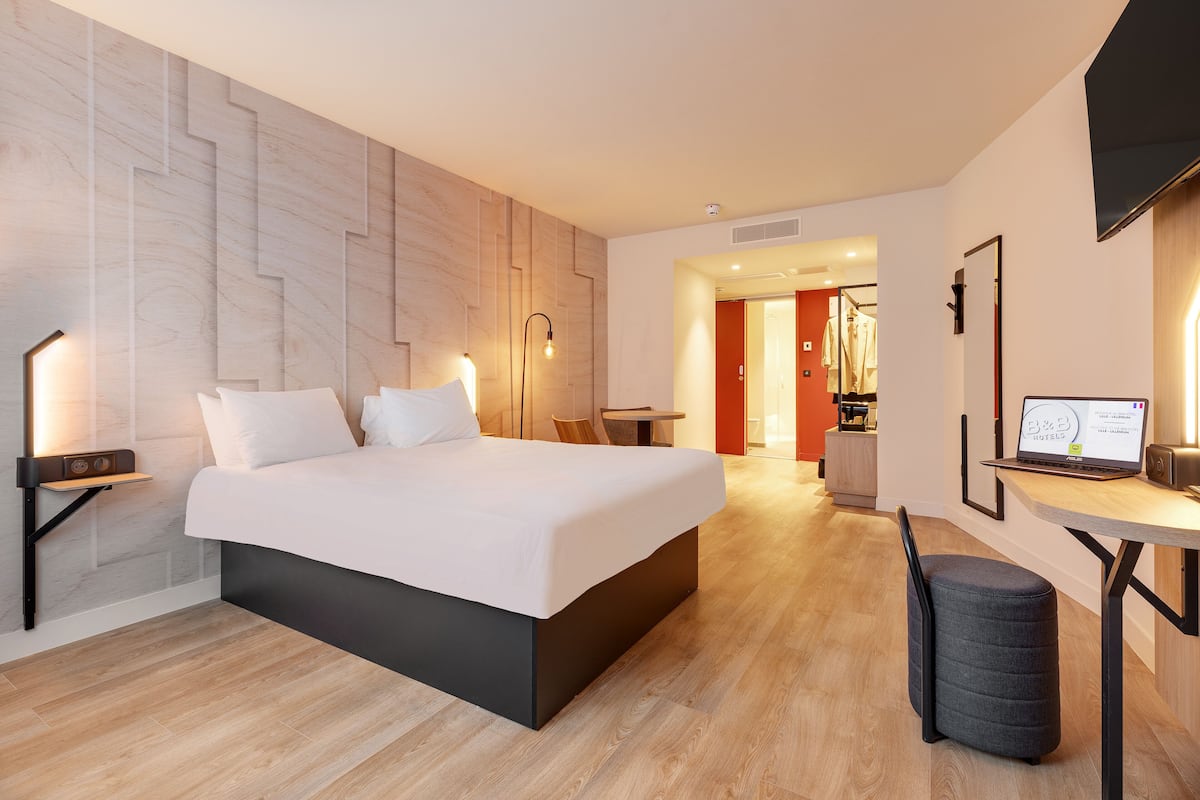 Moderni hotellihuone, jossa on suuri sänky, yöpöydät, työpöytä kannettavalla tietokoneella ja televisio.