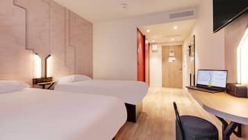 Habitación de hotel con dos camas, un escritorio con una computadora portátil, una silla y un televisor montado en la pared.