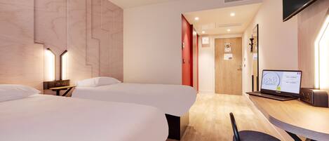 A hotel room with two beds, a desk with a laptop, a chair, and a TV mounted on the wall.