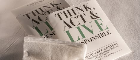 Un libro titulado "Think, Act & Live Responsibly" sobre una superficie blanca, con un objeto negro y una toalla blanca al fondo.