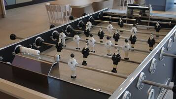 Una mesa de fútbol de mesa en una habitación con piso de madera, estructura metálica y figuras de jugadores en blanco y negro.