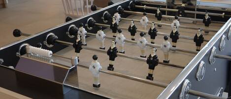 A foosball table in a room with a wooden floor, metal frame, and white and black player figures.