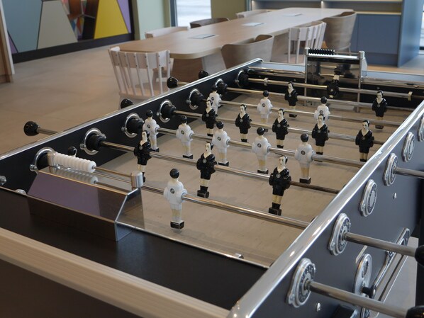 Una mesa de fútbol de mesa en una habitación con piso de madera, estructura metálica y figuras de jugadores en blanco y negro.