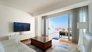A modern living room with a sofa, coffee table, and a flat-screen TV mounted on the wall. - Penthouse Triplex com Jacuzzi |T3 HsRentals Vilama (Vilamoura)