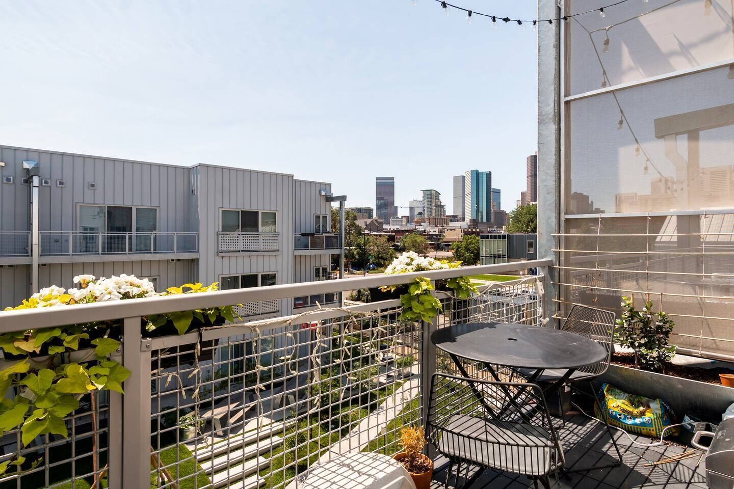 Terraza en la azotea con mesa y sillas, rodeada por una barandilla metálica y plantas en macetas.
