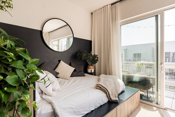 Un dormitorio moderno con una cama, un espejo redondo, una planta en maceta y vistas al exterior.