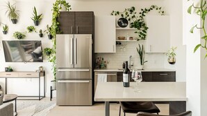 Eine moderne Küche mit Einbaukühlschrank, einem Esstisch mit Stühlen, einem an der Wand befestigten Fernseher und mehreren Zimmerpflanzen.