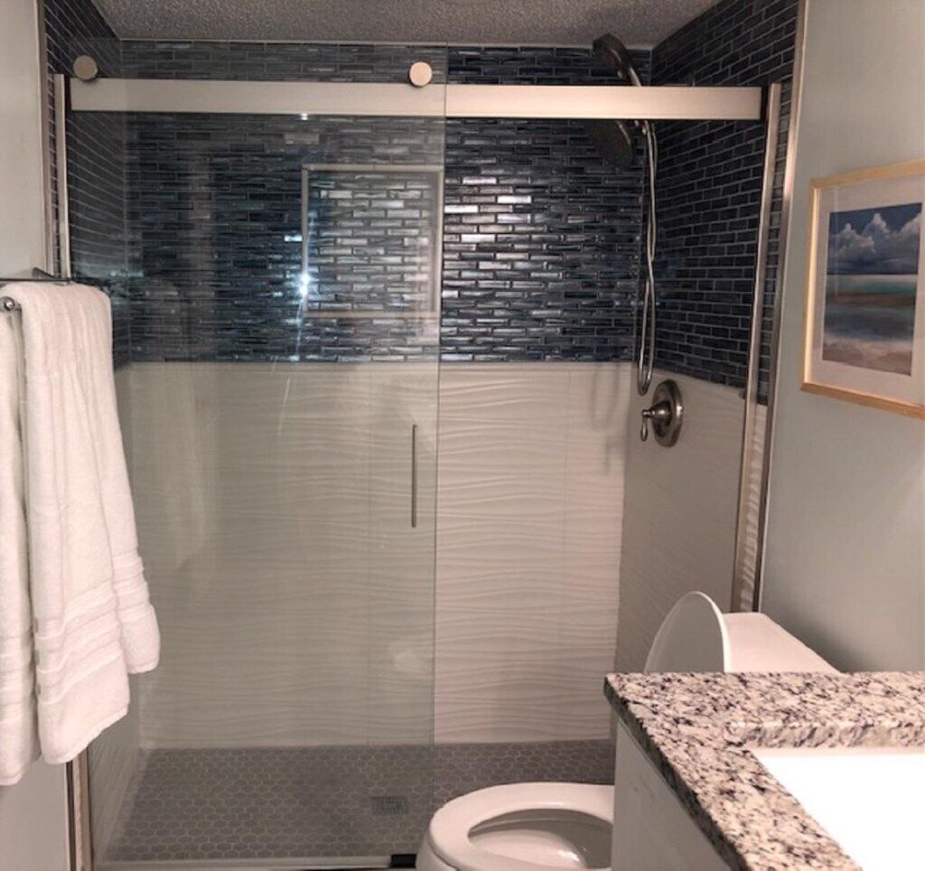 Une salle de bain moderne avec une douche à parois de verre, des toilettes blanches et un comptoir en granit.