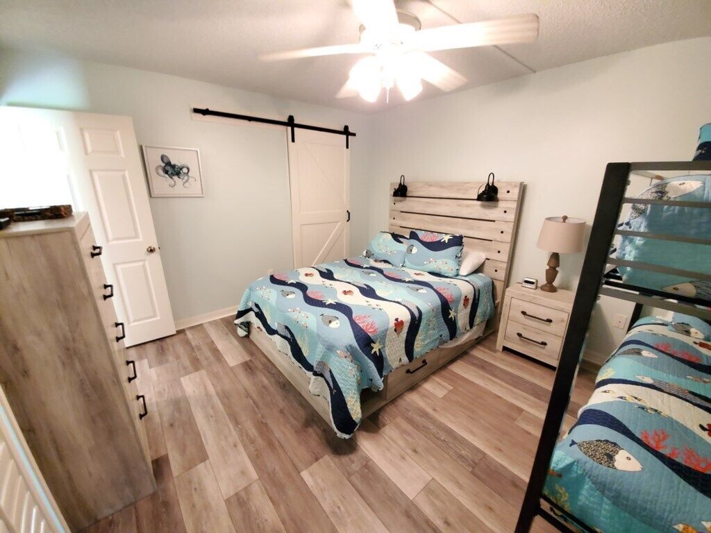 A bedroom with a bed, a dresser, a nightstand, and a ceiling fan.