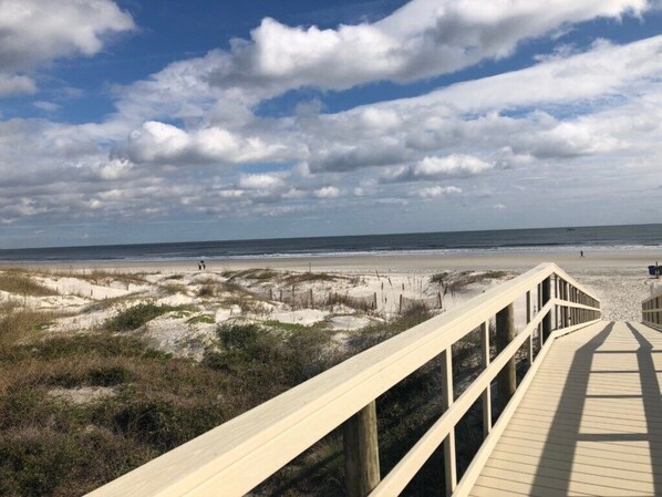 A wooden boardwalk leading to a beach with sand dunes and a clear sky. - Anastasia 112 (St. Augustine)