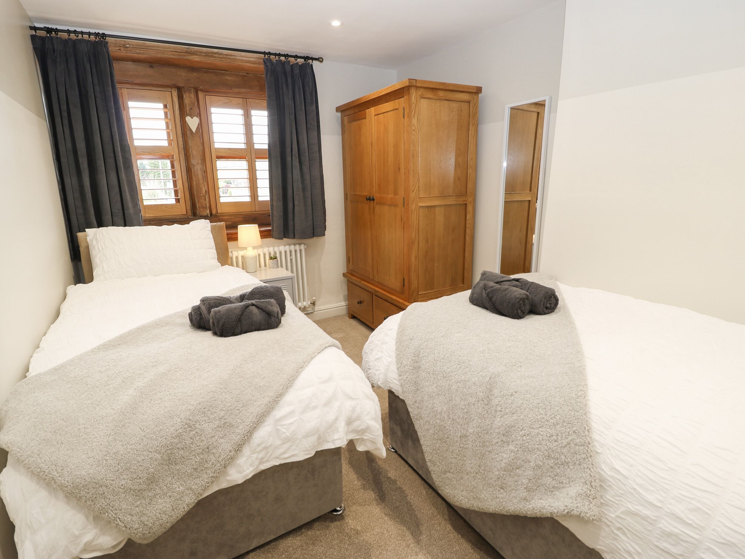 Une chambre avec deux lits, une armoire en bois, un radiateur et une fenêtre avec des rideaux.