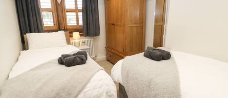 Une chambre avec deux lits, une armoire en bois, un radiateur et une fenêtre avec des rideaux.