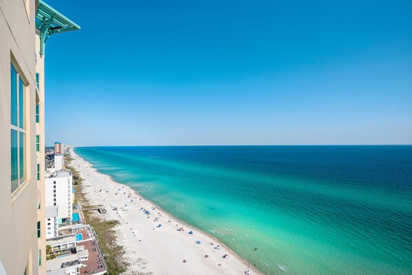 Une vue sur la plage depuis un immeuble de grande hauteur, avec une eau turquoise cristalline et une plage de sable.