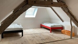 Een kleine zolderkamer met twee bedden, houten balken, een dakraam en een radiator.