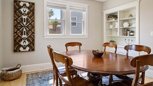 A dining room with a wooden table, chairs, a decorative wall piece, a window, and a white shelving unit.