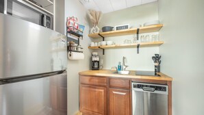 Eine kompakte Küche mit Edelstahlkühlschrank, Holzschränken, Geschirrspüler und Kaffeemaschine.