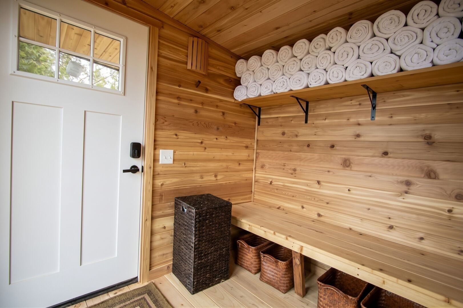 Un sauna con paredes de madera, un banco y un estante con toallas enrolladas.