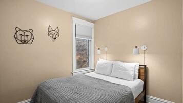 A bedroom with a bed, a window with a view of a brick wall, and two wall-mounted light fixtures.