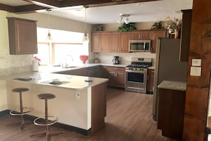 A kitchen with a central island, bar stools, stainless steel appliances, and wooden cabinets.