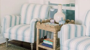 A striped sofa with a wicker side table holding books and a vase.