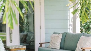 A wooden deck with a light blue sofa and a chair, a small table, and a glass door leading to a covered area.