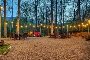 An outdoor seating area with tables and chairs, surrounded by trees and a gravel ground.