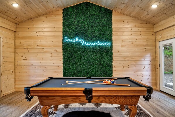 A pool table with a neon sign reading "Smoky Mountains" in a wooden room with a green wall.