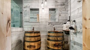 Un baño rústico con barriles de madera como lavamanos, una pared de madera y un espejo.