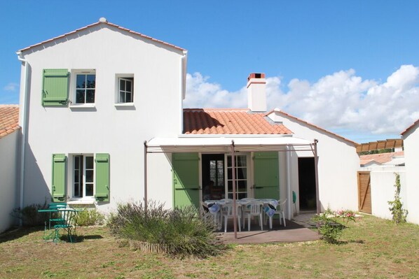 A two-story house with a covered patio area, a small garden, and a table set up outside.